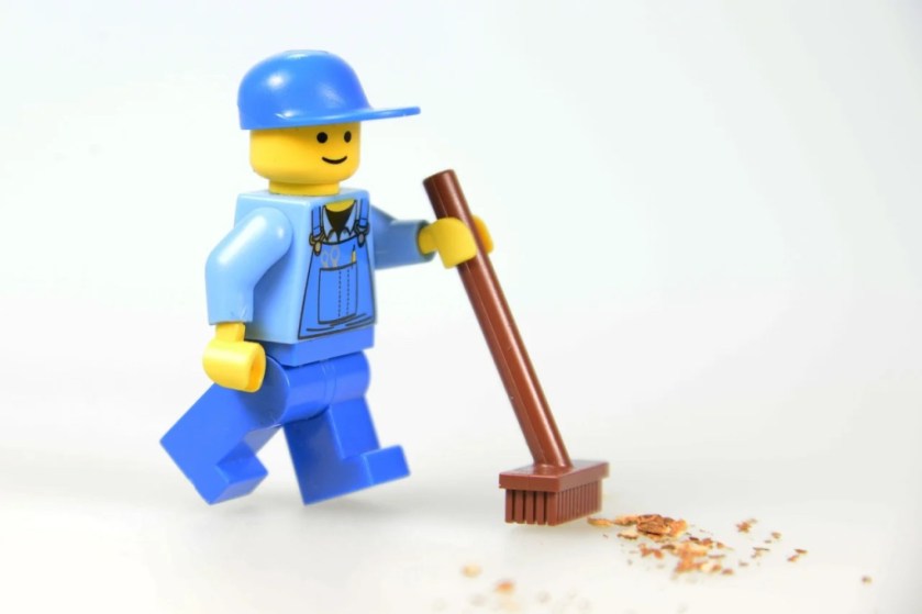 Lego mini figure with a broom sweeping up sawdust
